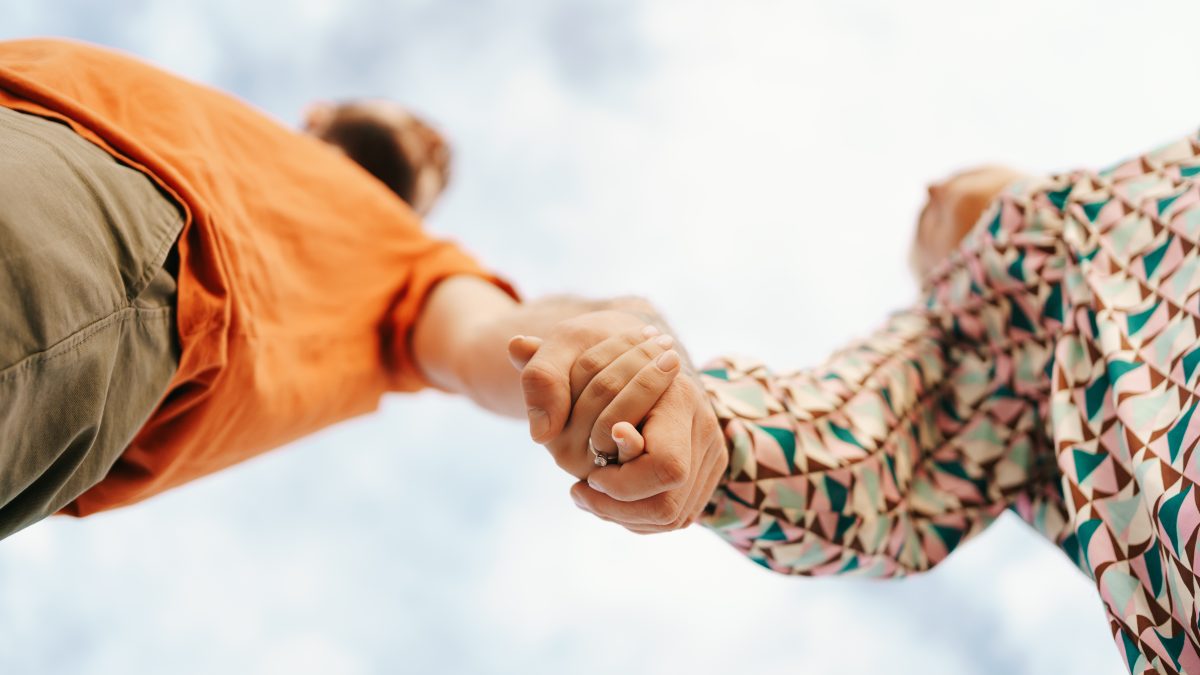 casal pegando nas mãos com céu ao fundo